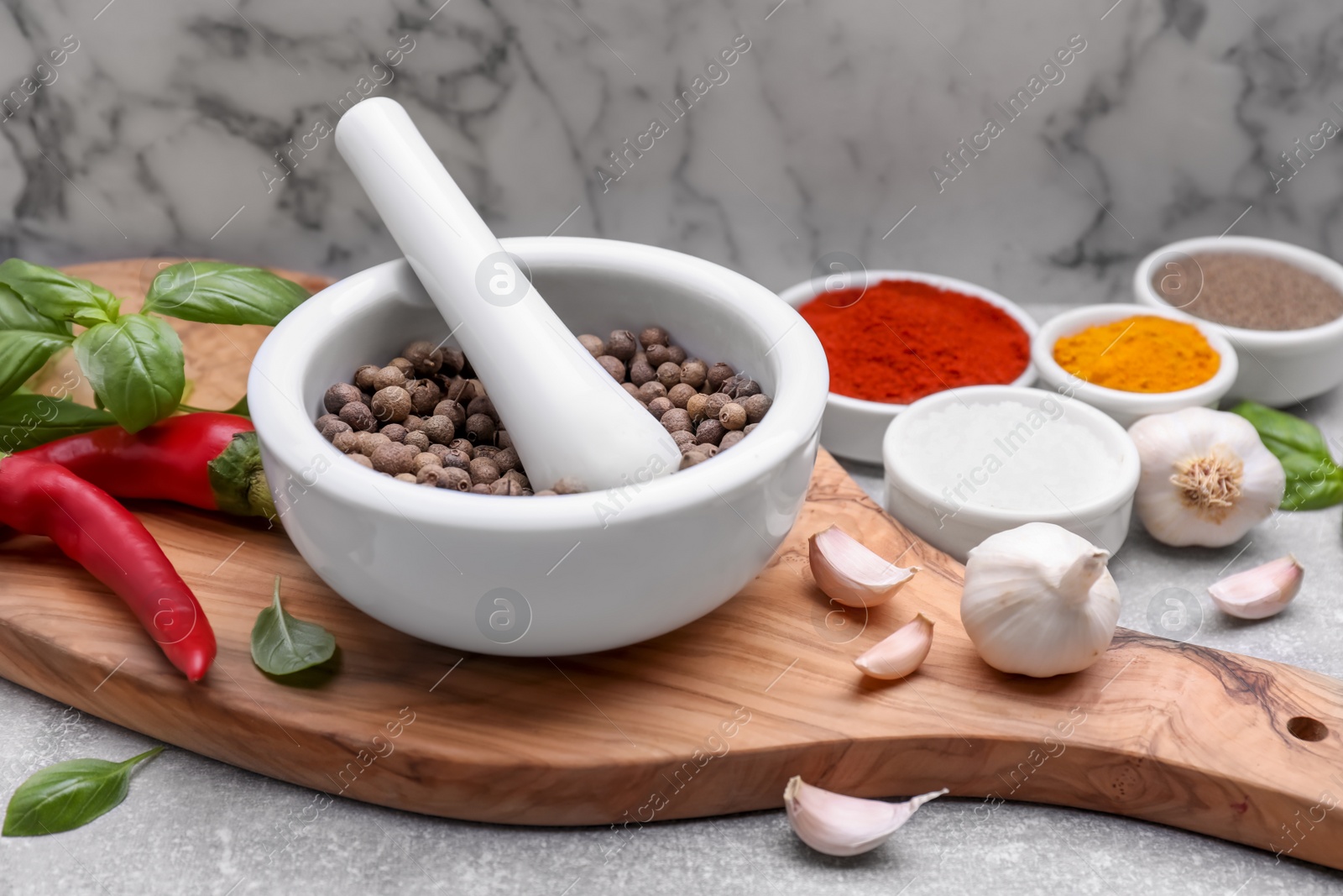 Photo of Mortar with pestle and different spices on light grey table against white marble wall