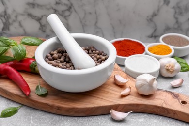 Photo of Mortar with pestle and different spices on light grey table against white marble wall