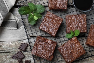 Photo of Cooling rack with delicious chocolate brownies and fresh mint on wooden table, flat lay