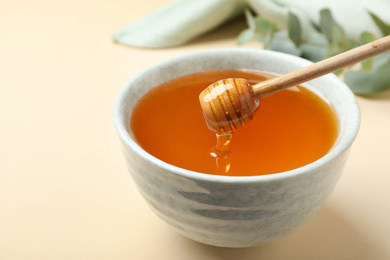 Photo of Bowl of organic honey and dipper on beige background