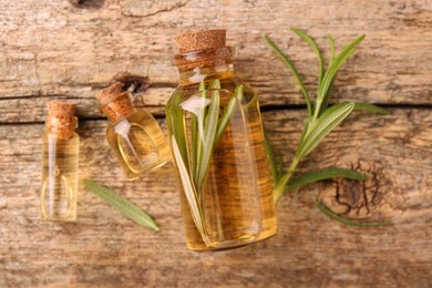 Aromatic essential oils in bottles and rosemary on wooden table, flat lay