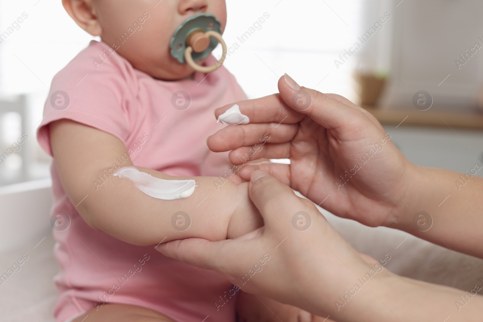 Photo of Mother applying body cream on her little baby at home, closeup