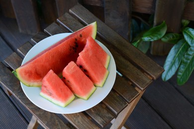 Photo of White plate with sliced watermelon on wooden stool outdoors. Space for text