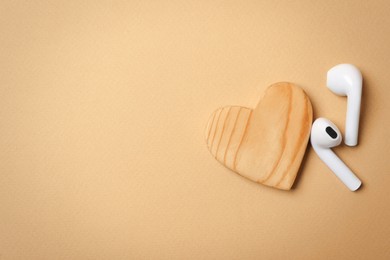 Photo of Modern earphones and heart on beige background, flat lay with space for text. Listening love music songs
