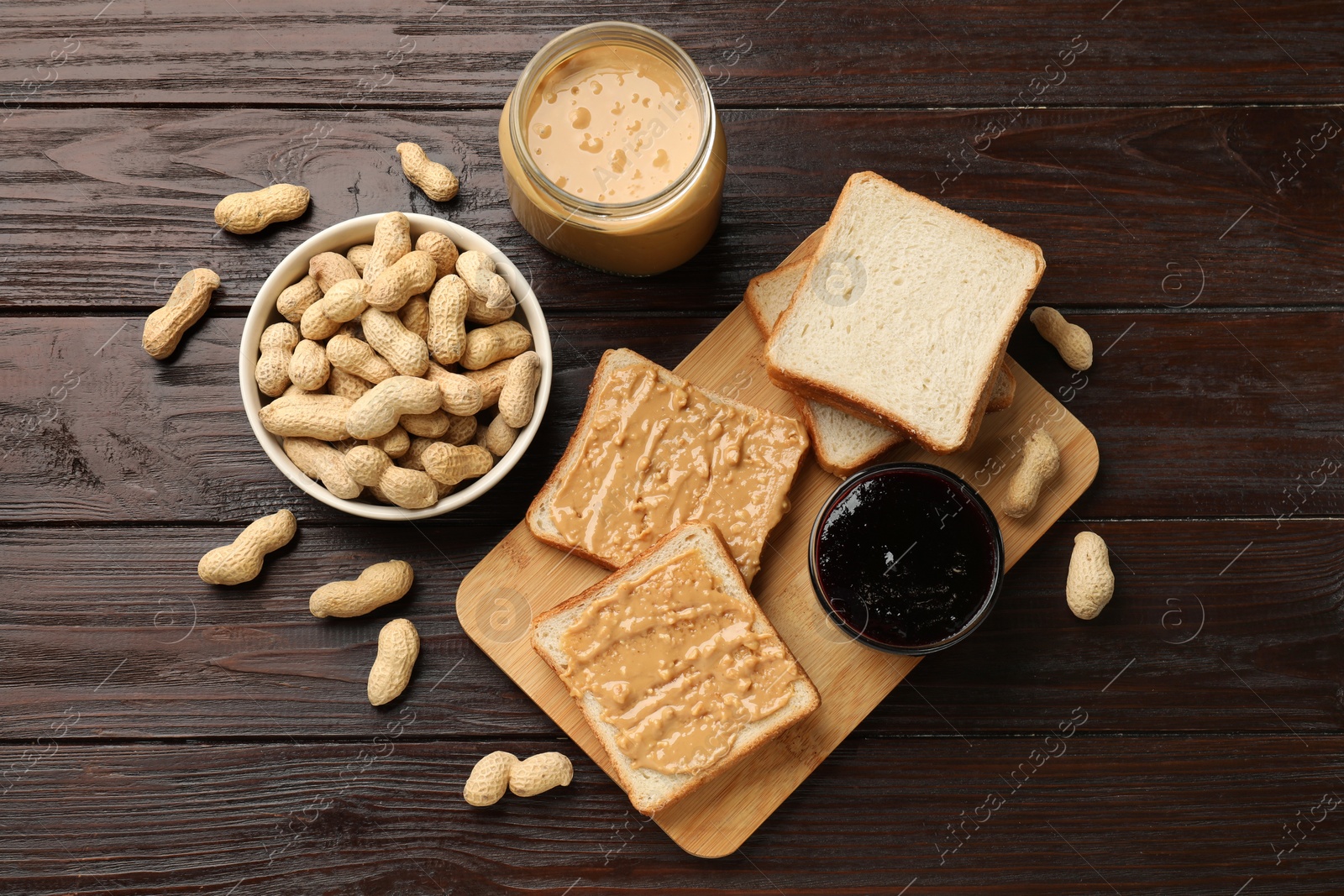 Photo of Delicious toasts with peanut butter, nuts and jam on dark wooden table, flat lay