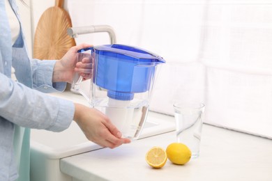 Photo of Woman with water filter jug in kitchen, closeup