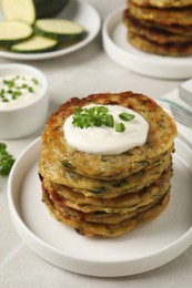 Delicious zucchini pancakes with sour cream served on light grey table