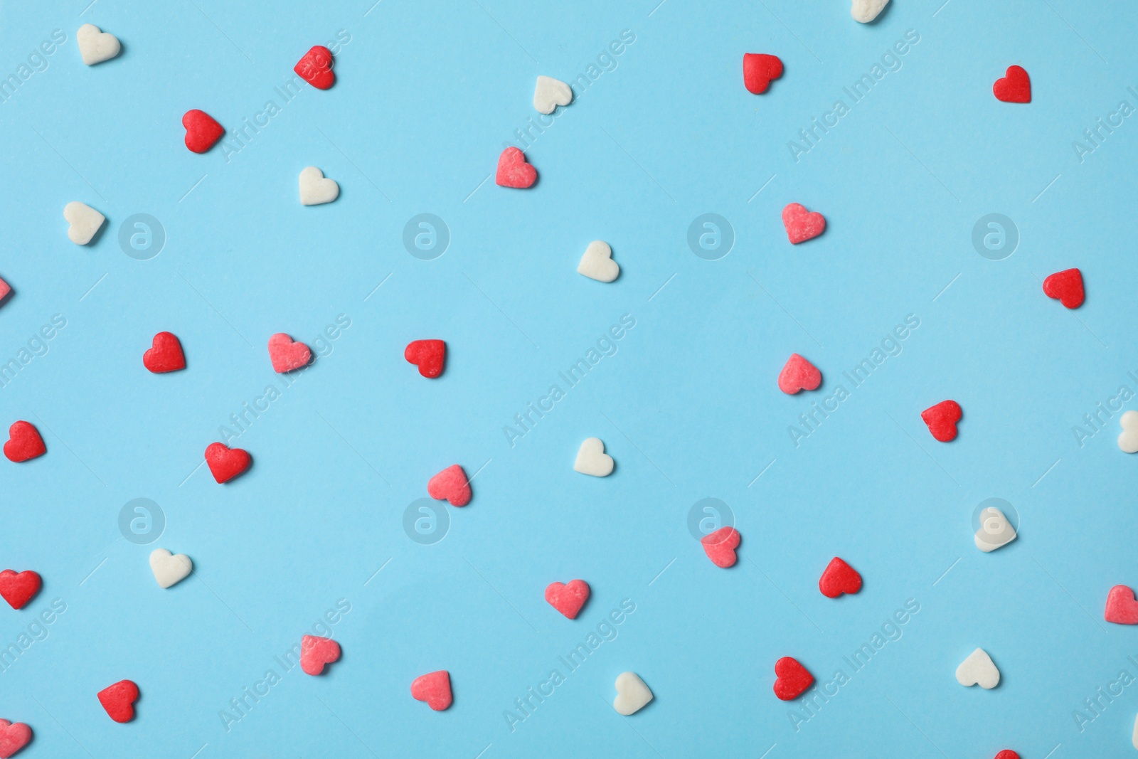 Photo of Bright heart shaped sprinkles on light blue background, flat lay