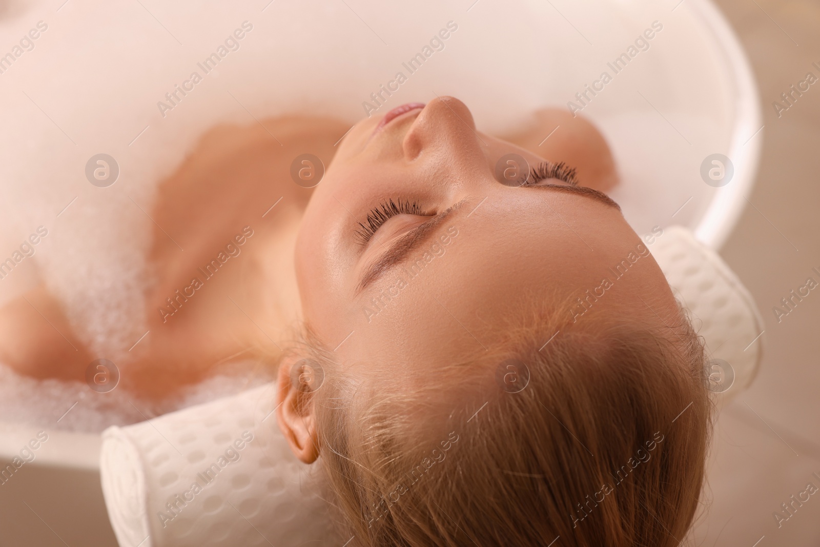 Photo of Young woman using pillow while enjoying bubble bath indoors, closeup