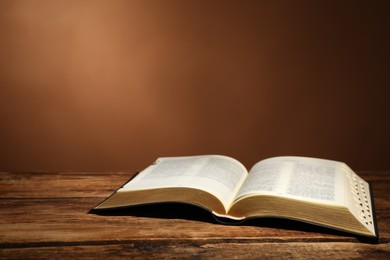 Open Bible on wooden table against brown background. Christian religious book