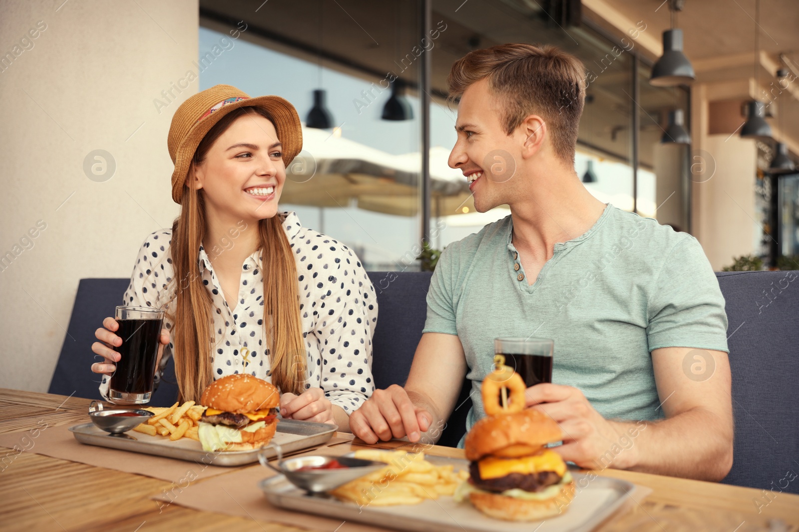 Photo of Young happy couple with burgers in street cafe