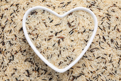 Photo of Mix of brown and polished rice with heart shaped bowl, top view