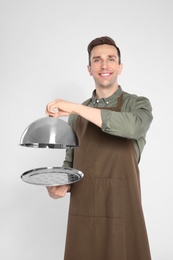 Photo of Handsome waiter holding metal tray with lid on light background