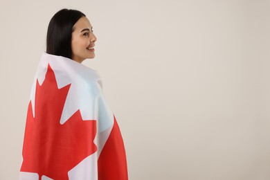 Photo of Happy young woman with flag of Canada on beige background, space for text