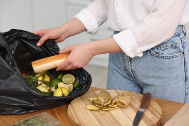 Photo of Garbage sorting. Woman putting food waste into plastic bag at wooden table indoors, closeup