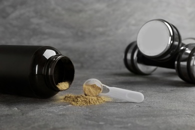 Jar and measuring spoon with hemp protein powder and dumbbells on table