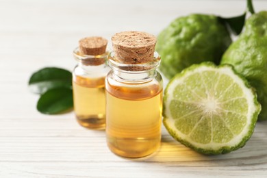 Photo of Glass bottles of bergamot essential oil on white wooden table, closeup