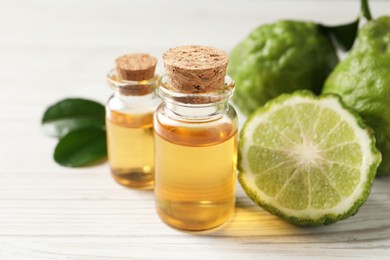 Glass bottles of bergamot essential oil on white wooden table, closeup