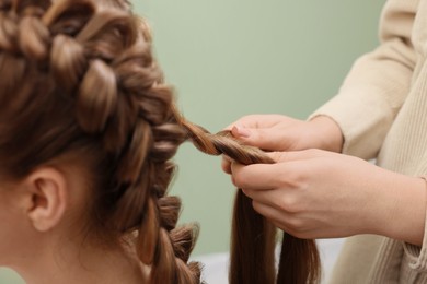 Photo of Professional stylist braiding woman's hair on olive background, closeup