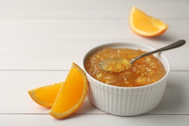 Photo of Delicious orange marmalade in bowl with spoon on white wooden table, space for text