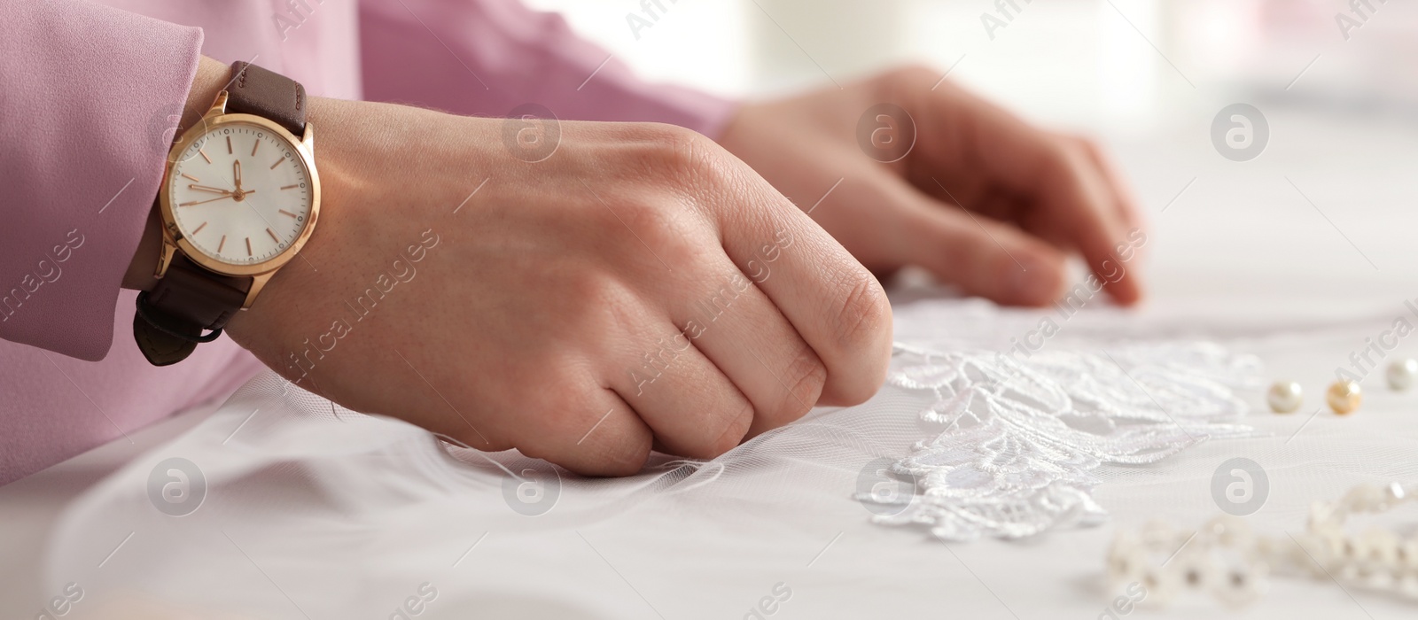 Image of Dressmaker working with white lace at table in workshop, closeup. Banner design