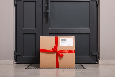 Photo of Christmas gift box on floor near door. Sending present by mail