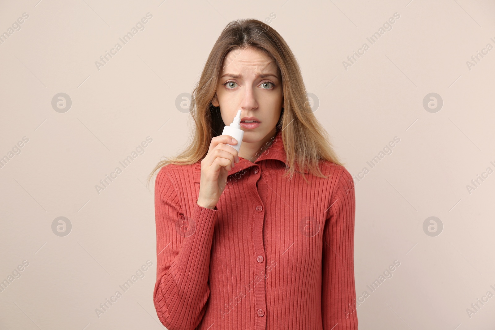 Photo of Sick young woman using nasal spray on beige background