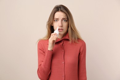 Photo of Sick young woman using nasal spray on beige background