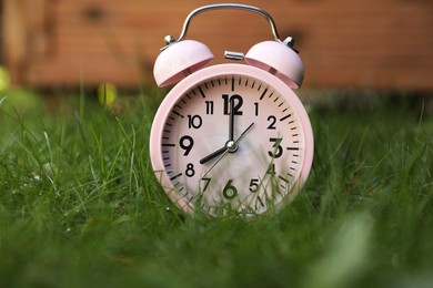Pink alarm clock on green grass outdoors