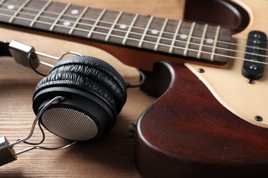 Photo of Modern electric guitar with headphones on wooden background, closeup view
