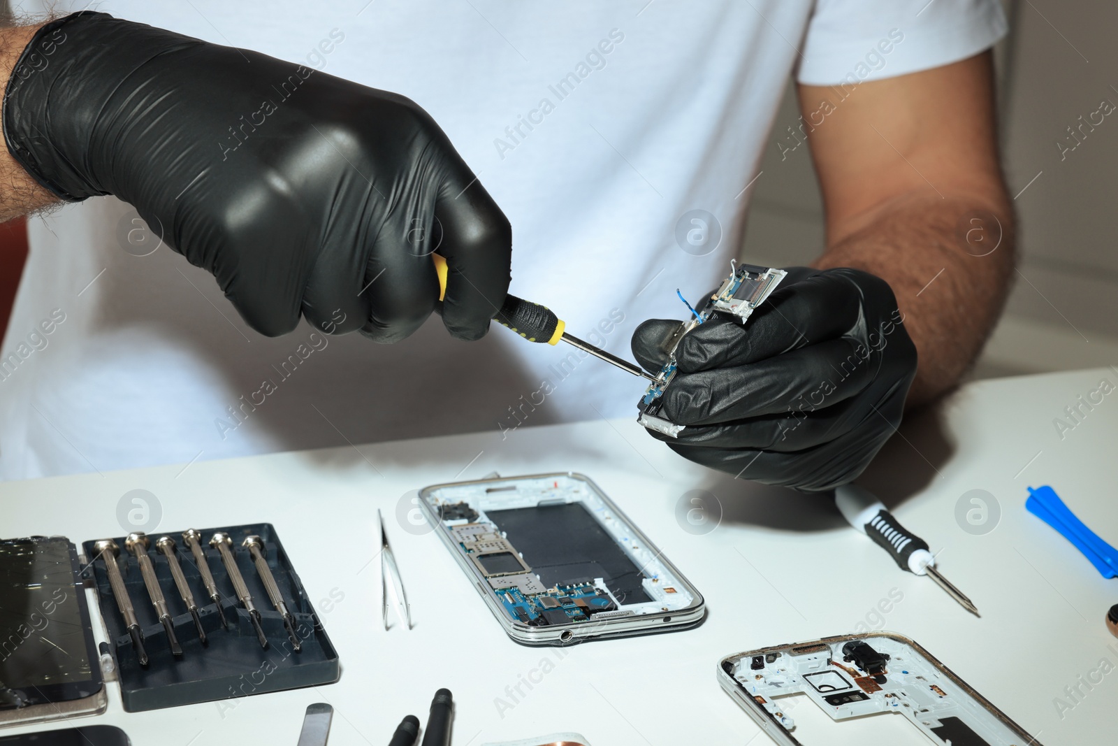 Photo of Technician repairing broken smartphone at white table, closeup