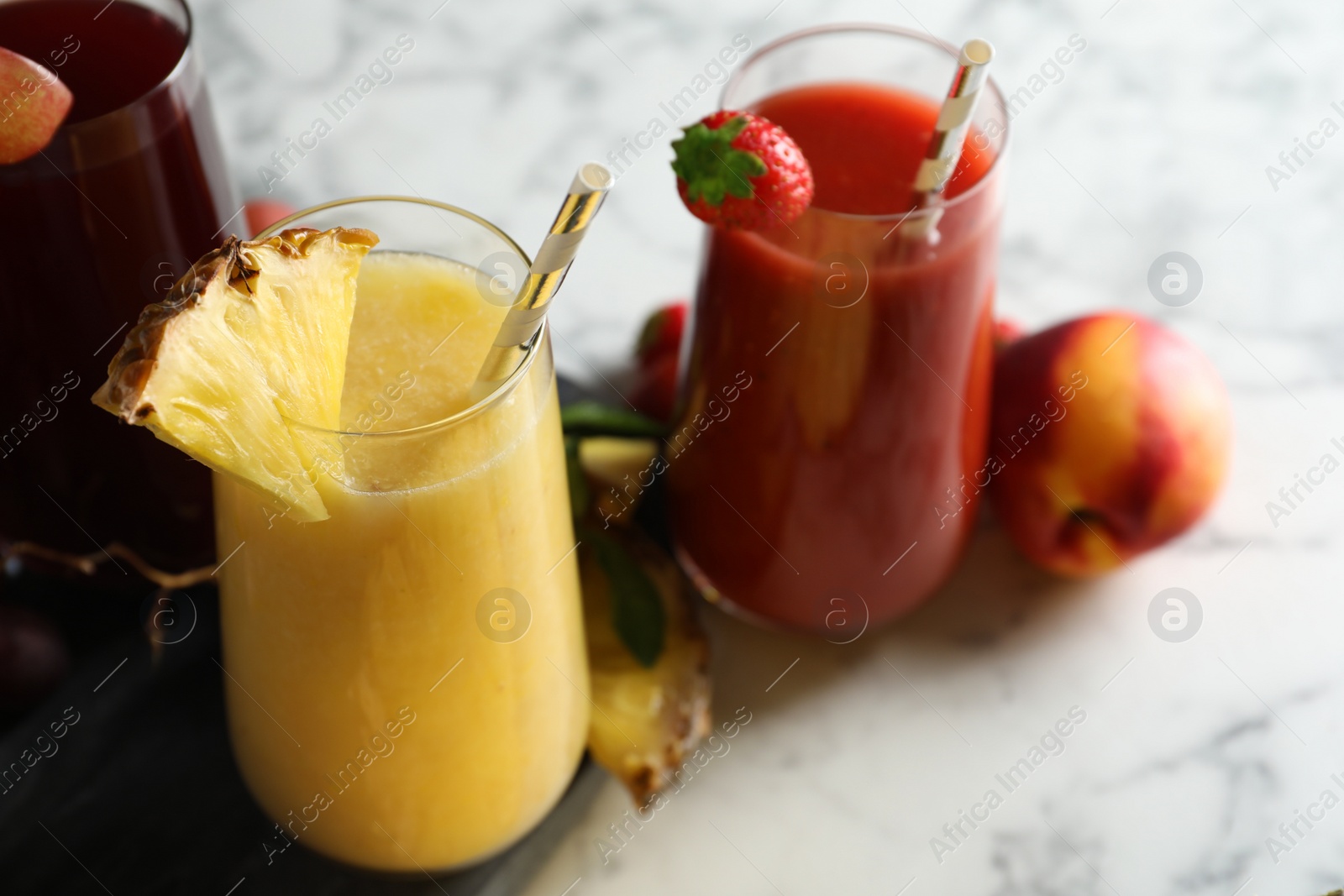 Photo of Glasses of delicious juices and fresh ingredients on white marble table, closeup