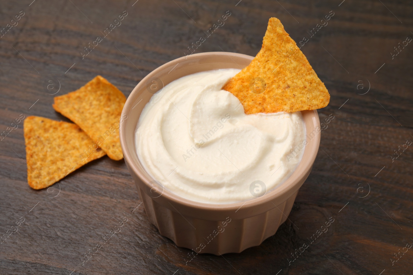 Photo of Delicious tofu sauce served with nachos chips in bowl on wooden table, closeup