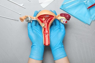 Gynecologist with anatomical model of uterus at light grey table, top view