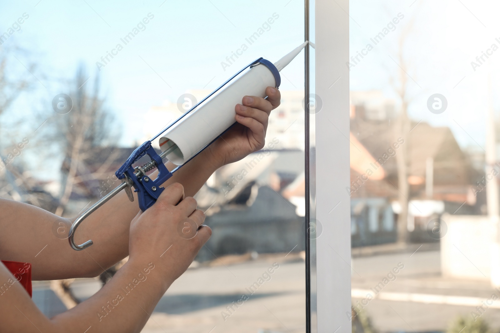 Photo of Construction worker sealing window with caulk indoors, closeup