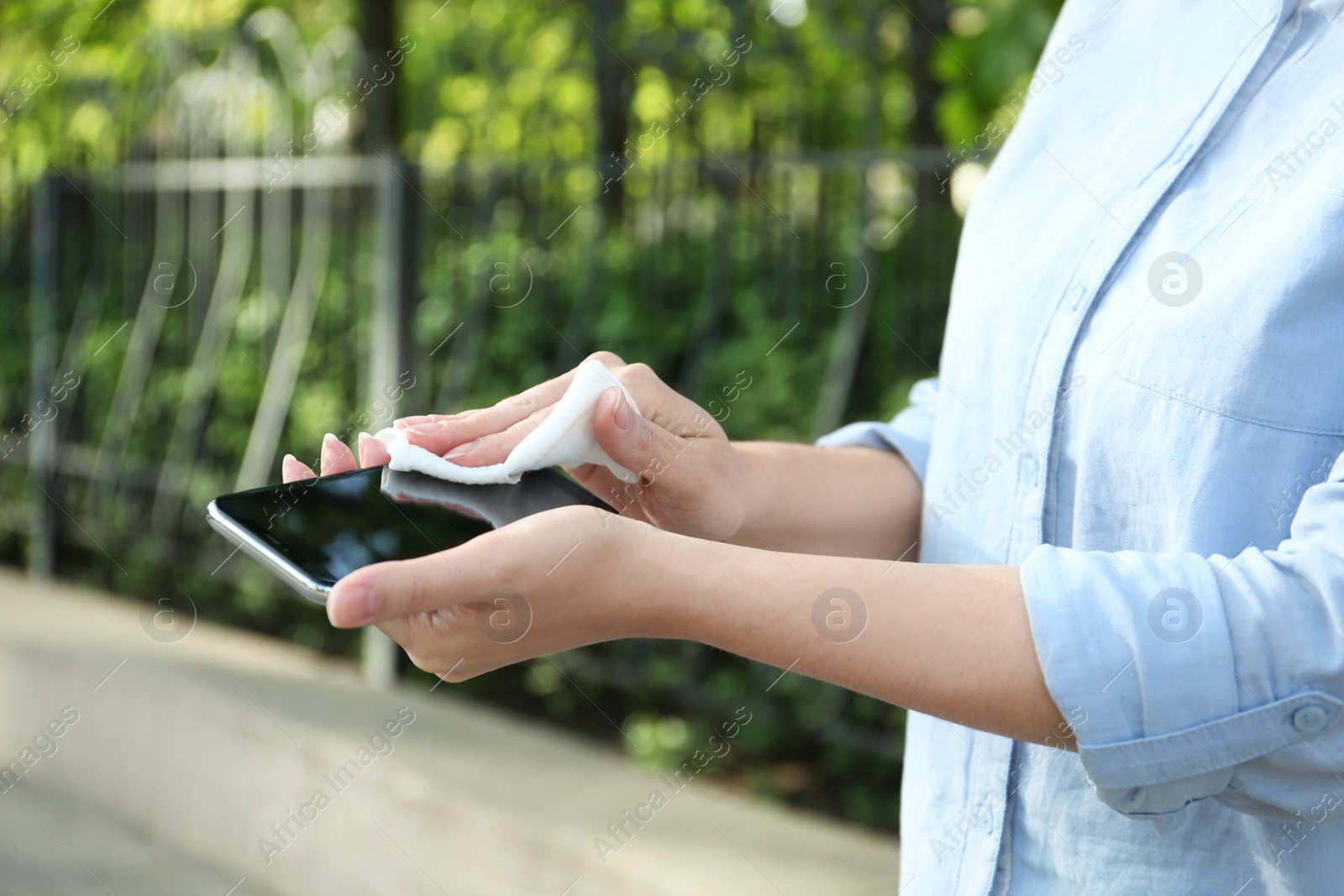 Photo of Woman cleaning smartphone with antiseptic wipe outdoors, closeup