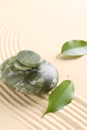 Photo of Zen garden stones and leaves on beige sand with pattern