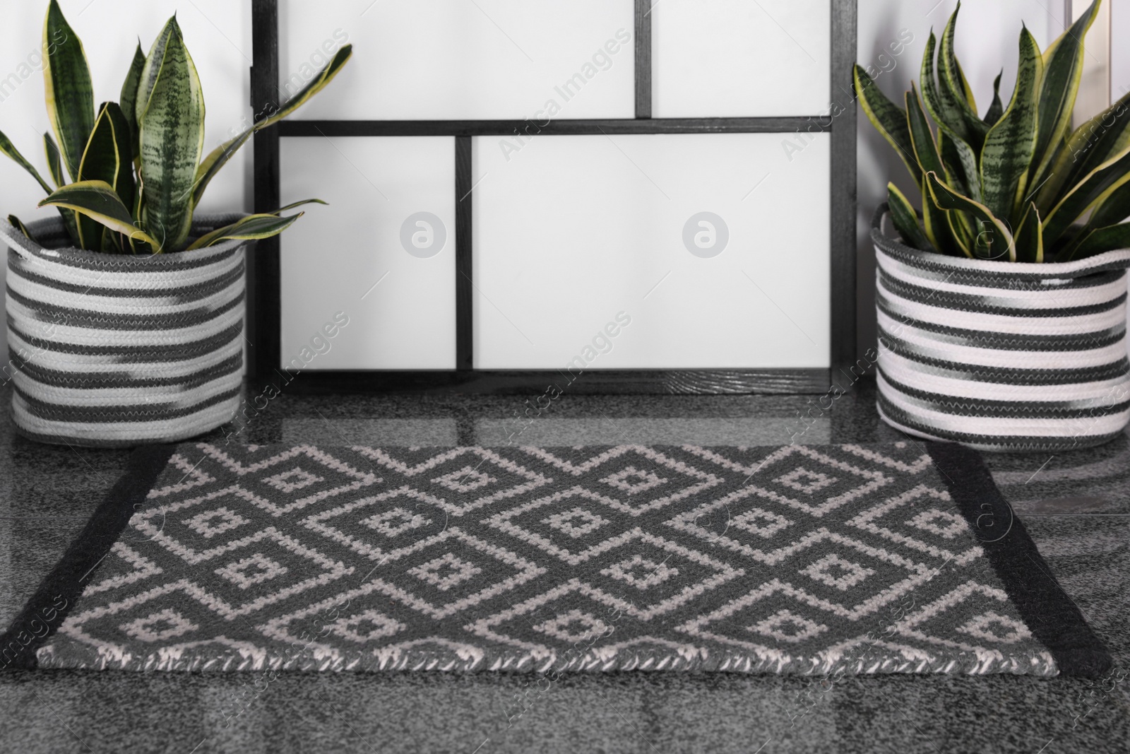 Photo of Stylish door mat with beautiful pattern and green houseplants on floor