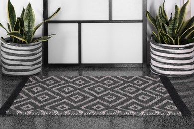 Photo of Stylish door mat with beautiful pattern and green houseplants on floor