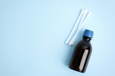 Photo of Bottle of medical iodine and cotton buds on light blue background, flat lay. Space for text