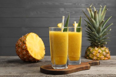 Photo of Tasty pineapple smoothie and cut fruit on wooden table