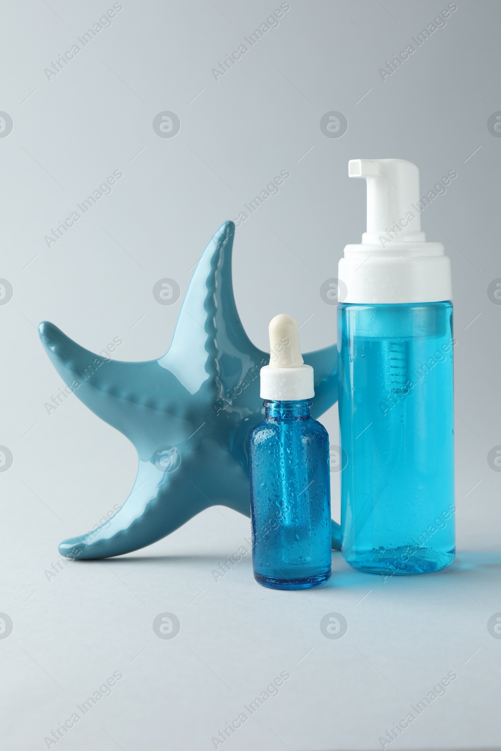 Photo of Bottles of cosmetic products and decorative starfish on light grey background