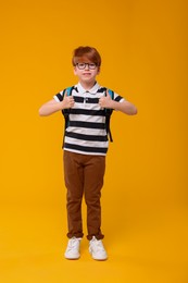 Photo of Happy schoolboy showing thumbs up on orange background
