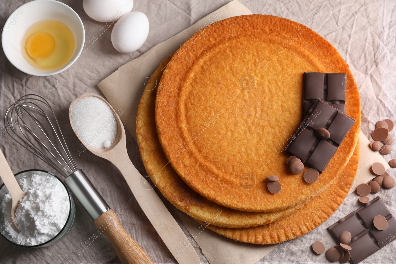 Photo of Delicious homemade sponge cakes and ingredients on grey tablecloth, flat lay