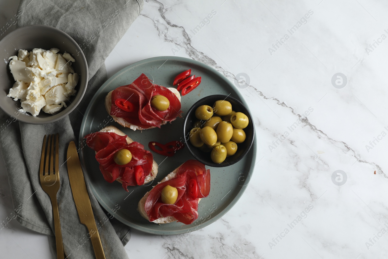 Photo of Delicious sandwiches with bresaola, cream cheese and olives served on white marble table, flat lay. Space for text