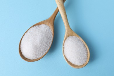 Photo of Organic white salt in spoons on light blue background, top view