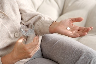 Senior woman with pill and glass of water indoors, closeup