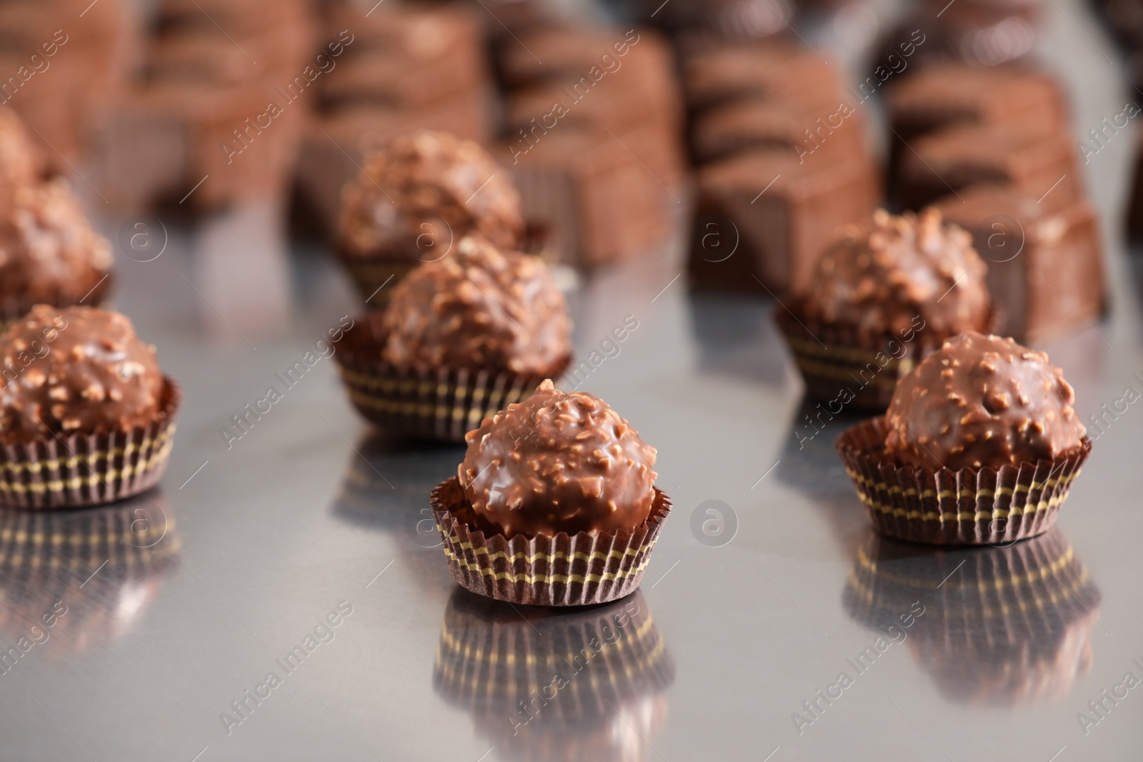 Photo of Many delicious chocolate candies on grey table. Production line