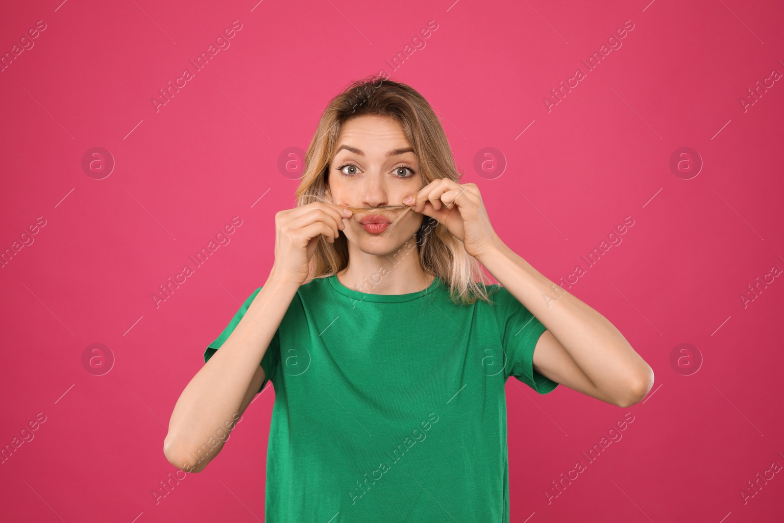 Photo of Funny woman making fake mustache with her hair on pink background