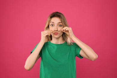 Funny woman making fake mustache with her hair on pink background